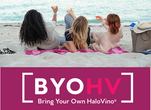 girls drinking wine on a beach with the hashtag BYOHV Bring your own HaloVino